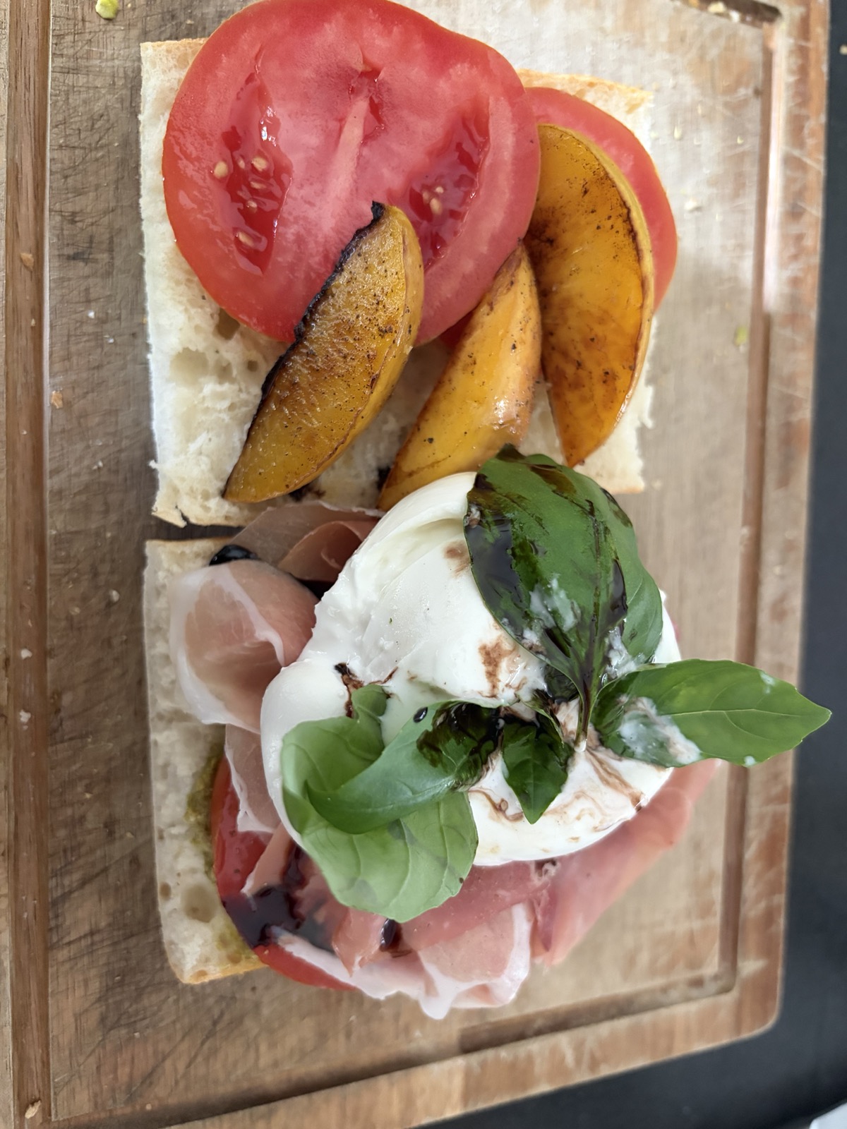 Broodje belegd met tomaat, gebakken nectarine, groene pesto, parmaham, burrata, verse basilicum en balsamico