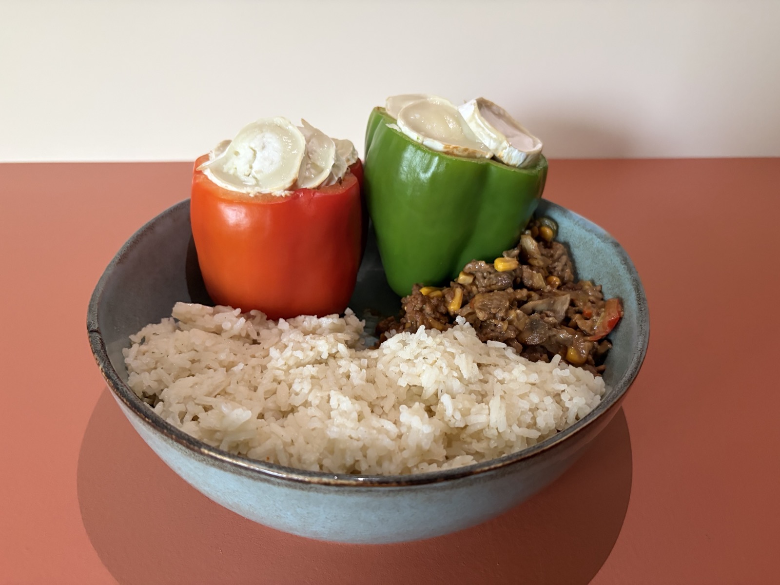 Twee gevulde paprika's op een rond bord, gevuld met gehakt en groentes, met rijst ernaast